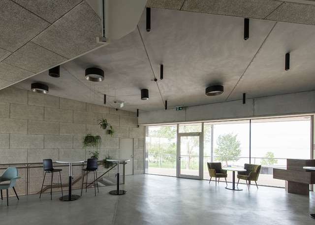 Modern interior with concrete ceiling featuring black cylindrical surface-mounted and pendant spotlights illuminating an open lounge area.