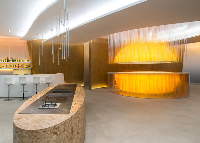 Interno di bar moderno con luci a sospensione su cavi sottili, bancone curvo dorato con tenda a frange e illuminazione d'atmosfera calda