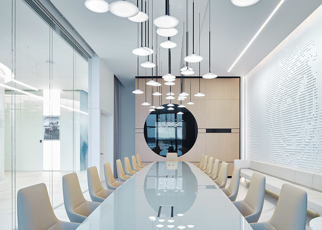 Sala conferenze moderna con gruppo di lampade a sospensione a disco bianco a diverse altezze su lungo tavolo bianco con sedie beige