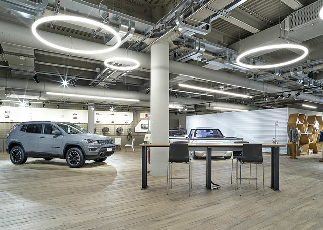 Car showroom lit by Artemide circular pendant lights, showcasing a Jeep Compass SUV and a consultation table.
