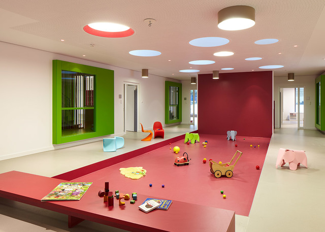 Colorful children's playroom with red platform, toys, and Artemide round ceiling lights illuminating the vibrant space