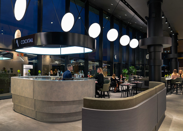 Bar cocktail moderno con lampada a sospensione circolare e pendenti a globo sferico bianco che illuminano le aree salotto e il bancone.