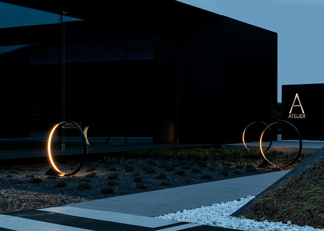 Due lampade da terra circolari Artemide per esterni con illuminazione ad arco LED caldo, installate in un'area d'ingresso paesaggistica al crepuscolo.