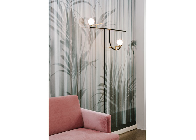 Black and brass floor lamp with two opal glass globe shades, placed beside a pink velvet sofa against a tropical wallpaper