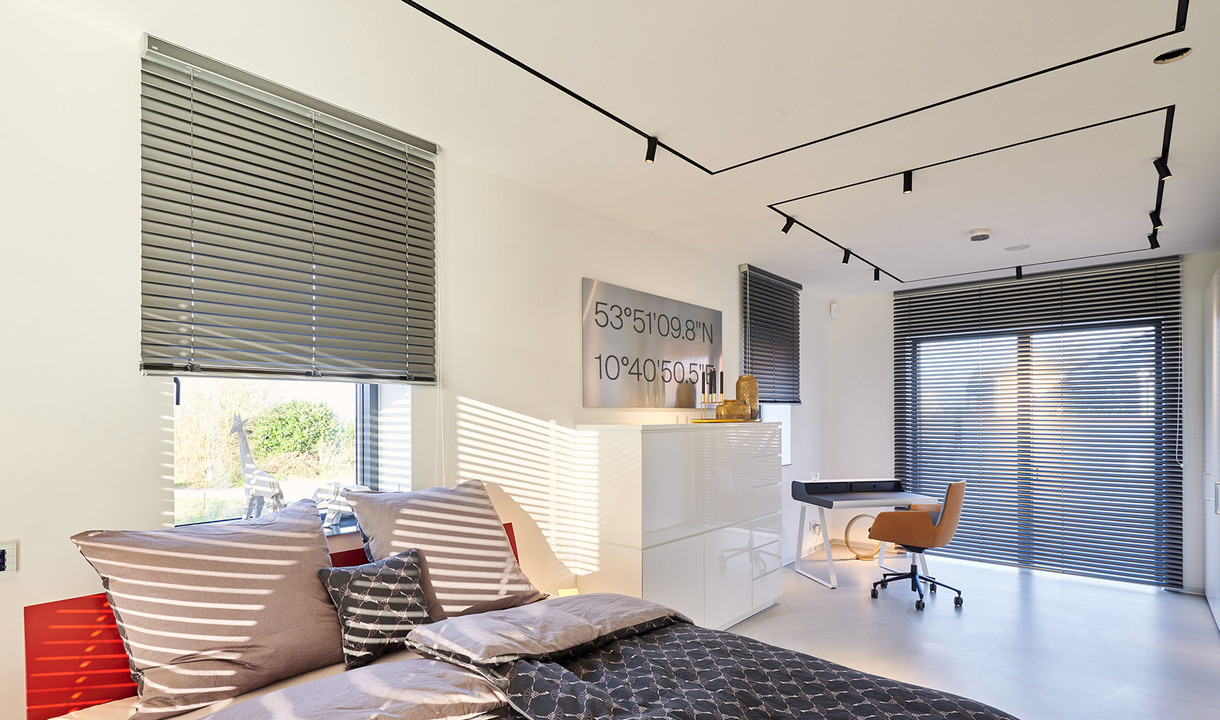 Camera da letto moderna con faretti Artemide su binario a soffitto, veneziane grigie, letto con cuscini e area scrivania