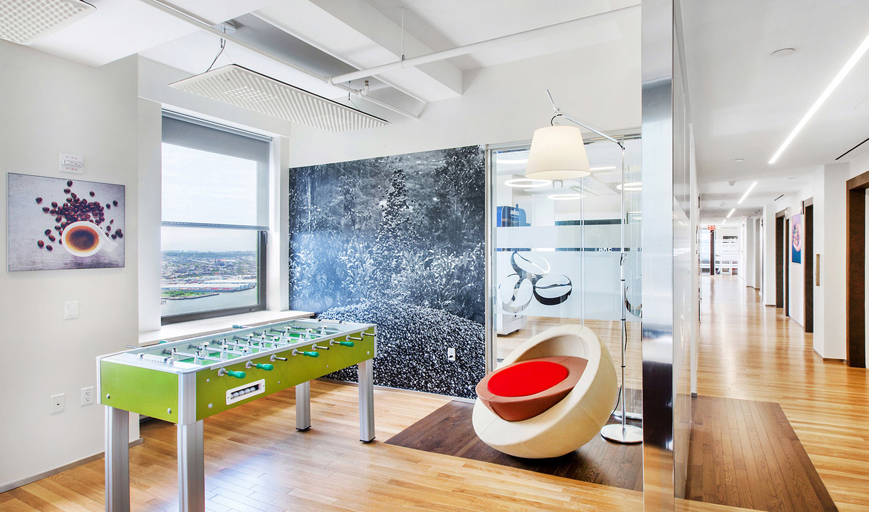 Sala relax ufficio moderna con calciobalilla, poltrona a bozzolo e lampada da terra Artemide Tolomeo Mega vicino a parete in vetro