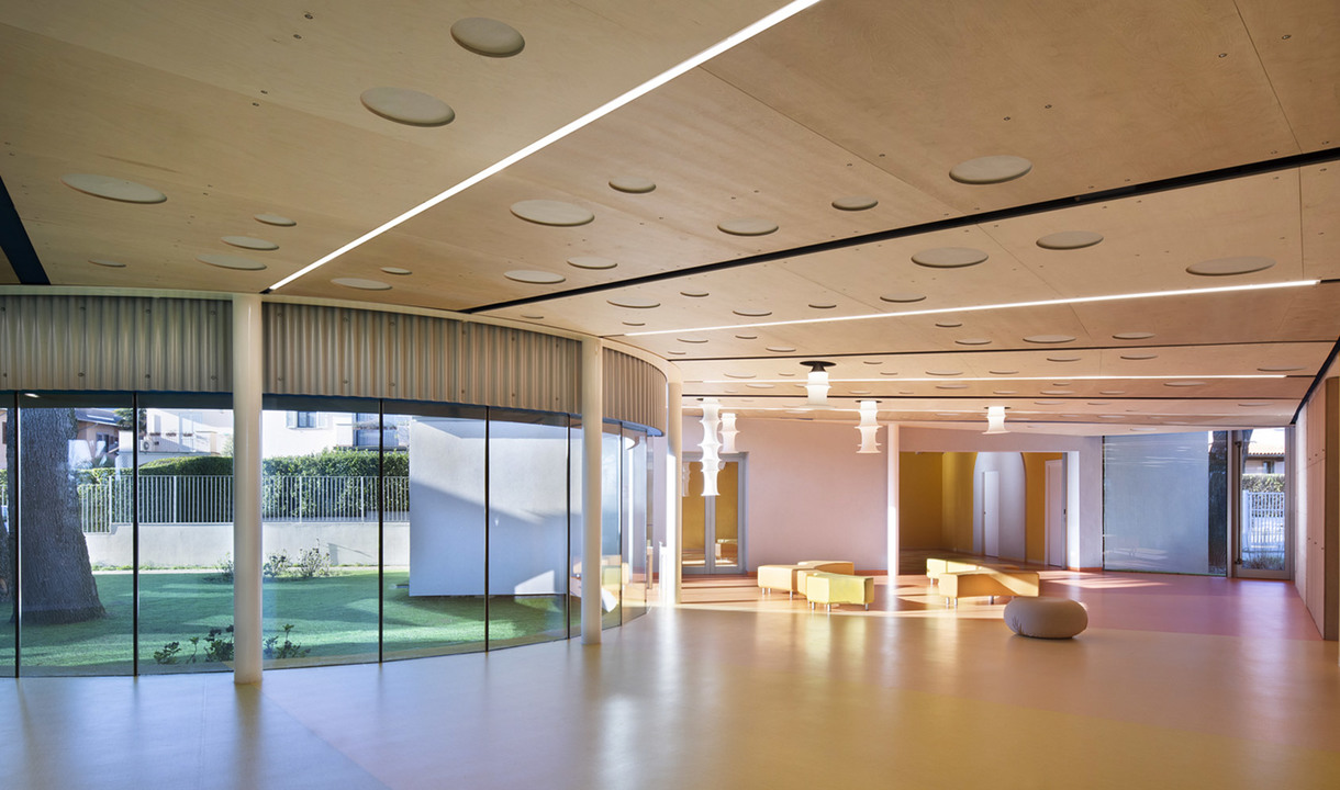 Ampio interno moderno con soffitto in legno caldo, illuminazione LED lineare a incasso, lampade a sospensione e pareti vetrate dal pavimento al soffitto con vista sul giardino