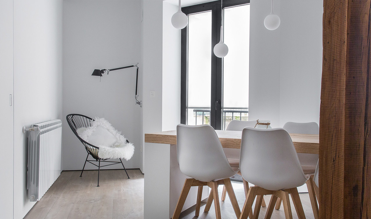 Zona pranzo minimalista con sedie tulip bianche, tavolo in legno, due lampade a sospensione a globo bianco e una lampada da lettura vicino a una poltrona.