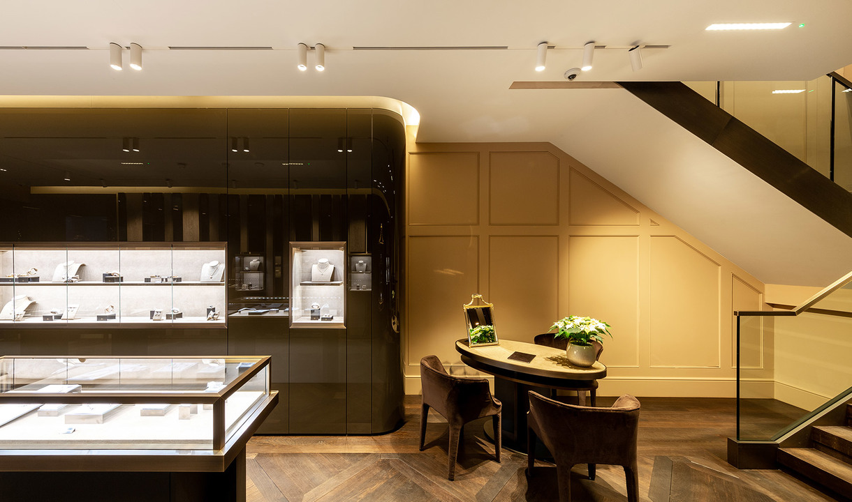 Elegant jewelry store interior with Artemide track spotlights illuminating display cases and a consultation table with chairs.