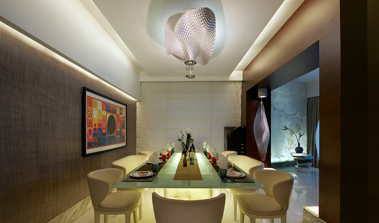 Sala da pranzo elegante con un grande lampadario scultoreo dal paralume metallico intrecciato, che illumina un tavolo in vetro con sedie color crema.