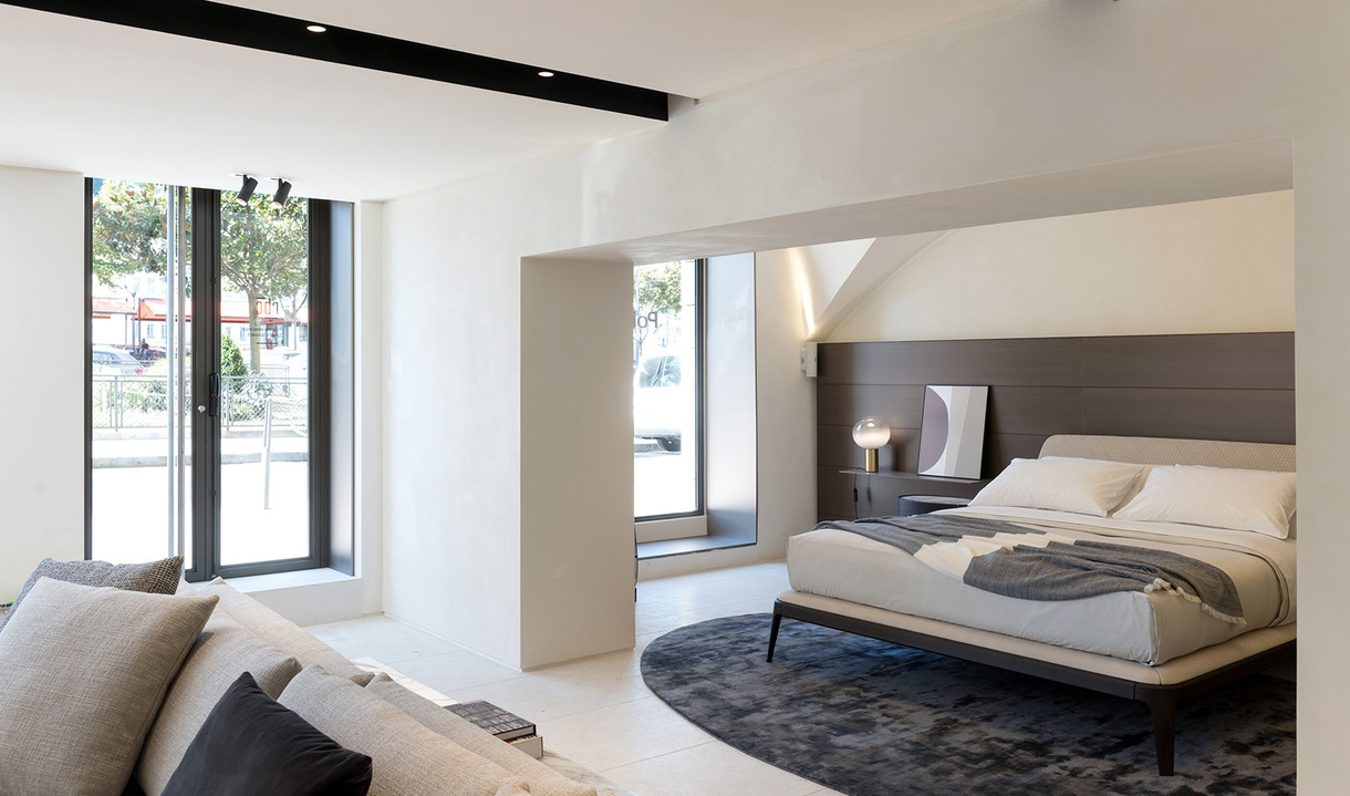 Camera da letto moderna con design minimalista, lampada da tavolo sul comodino, pareti bianche, testiera scura e tappeto circolare scuro