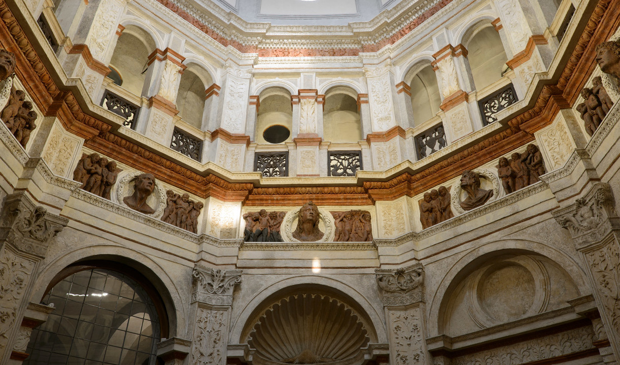 Ornate interior of a historic building featuring multi-tiered marble arches, decorative friezes, sculpted busts, and terracotta details