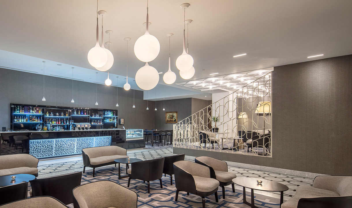 Elegante lounge di hotel con lampade a sospensione a globo Artemide di varie dimensioni, che illuminano zona salotto, bancone bar e scala decorativa.