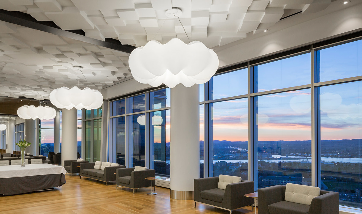 Modern lobby with large cloud-shaped white pendant lights hanging over seating areas, floor-to-ceiling windows with sunset view