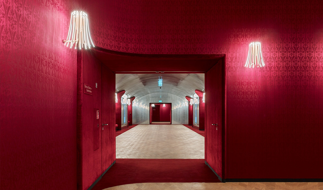 Red damask corridor with Artemide wall sconces featuring cascading tubular neon lights, leading to a vaulted hallway