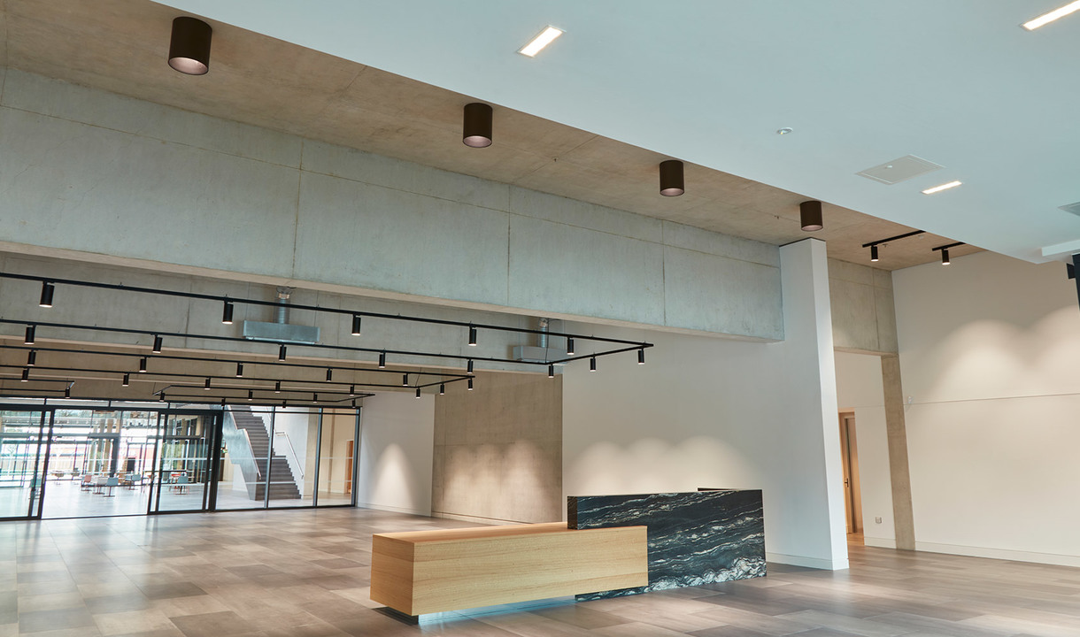 Ingresso moderno con faretti cilindrici a soffitto, binari neri con faretti sul soppalco e reception bicolore su pavimento in legno