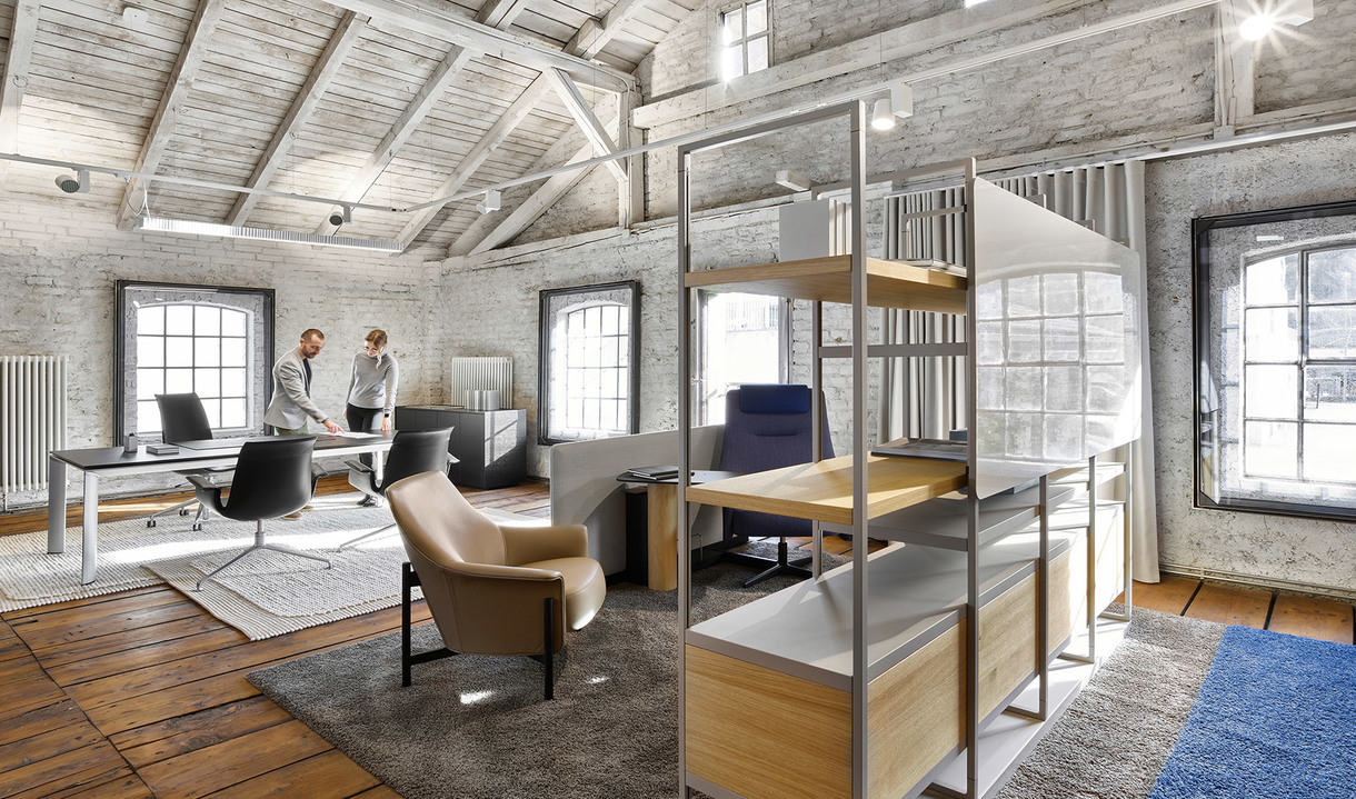 Ufficio loft moderno con pareti in mattoni a vista, travi in legno, libreria aperta, poltrona in pelle e due persone che lavorano alle scrivanie