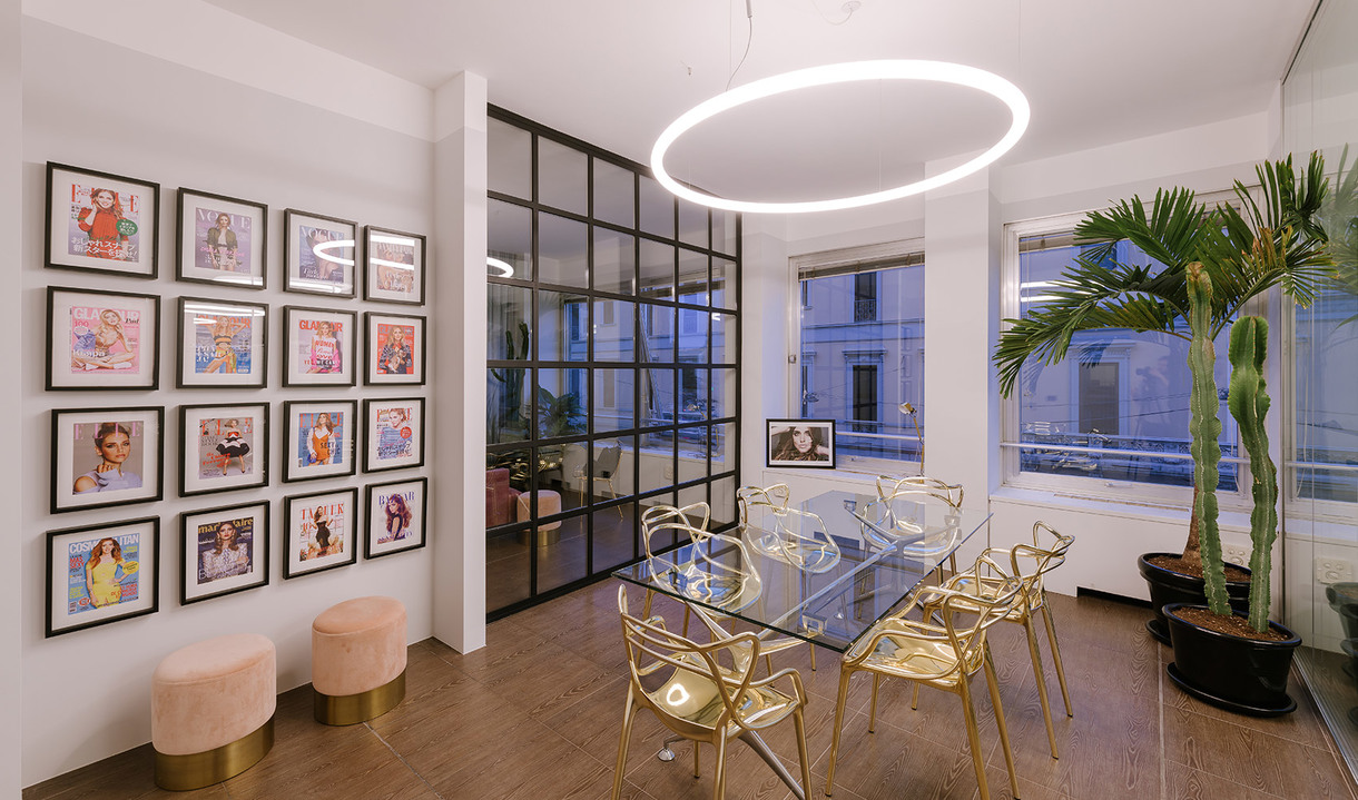 Modern meeting room with Artemide circular LED pendant light over a glass table with gold chairs, framed art wall, and indoor palm.