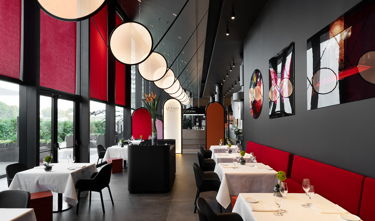 Interno di ristorante elegante con una fila di grandi lampade a sospensione sferiche bianche che illuminano una sala da pranzo con accenti rossi e pareti scure.