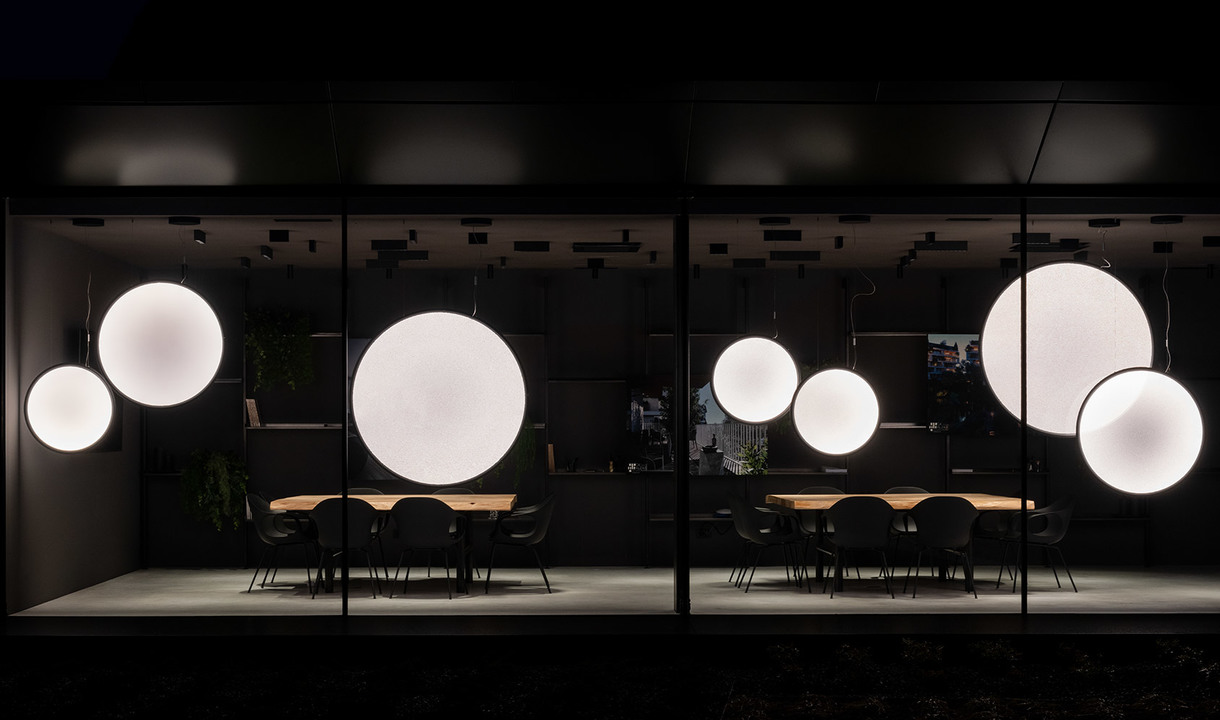 Showroom Artemide di notte: più lampade a sospensione sferiche bianche luminose di diverse dimensioni sospese su una sala da pranzo scura