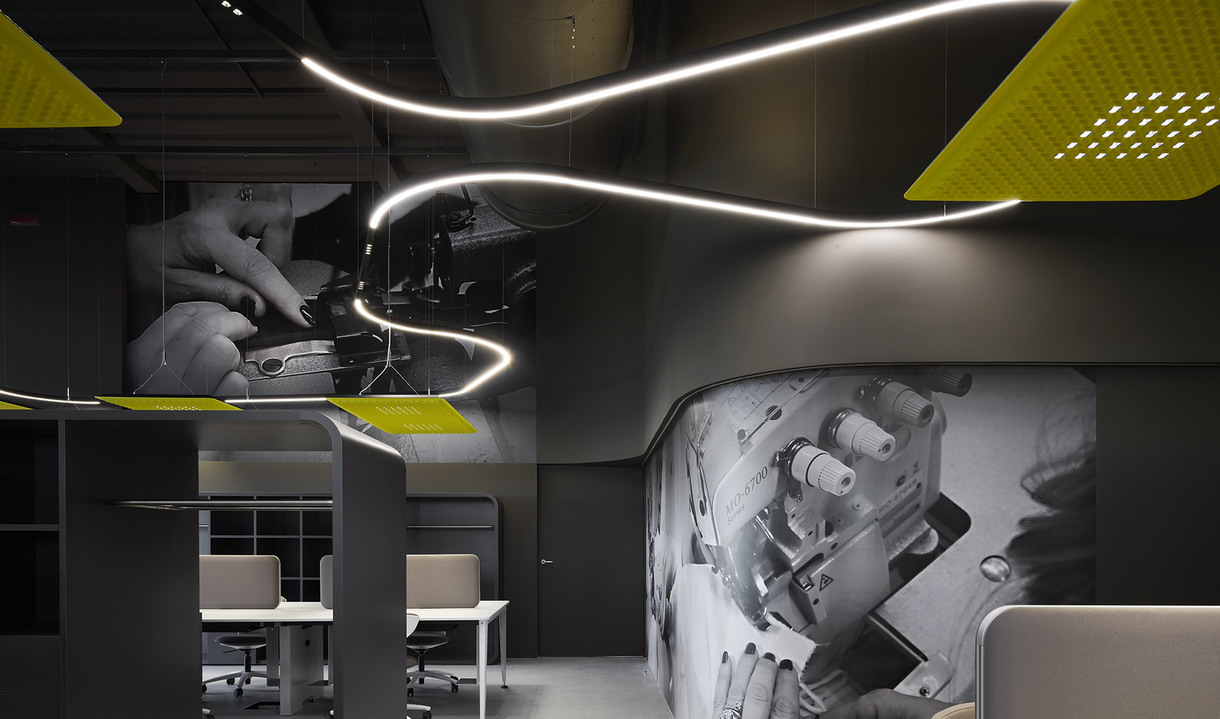 Modern office with Artemide sinuous LED pendant light creating fluid curves above workstations, complemented by yellow perforated ceiling panels.