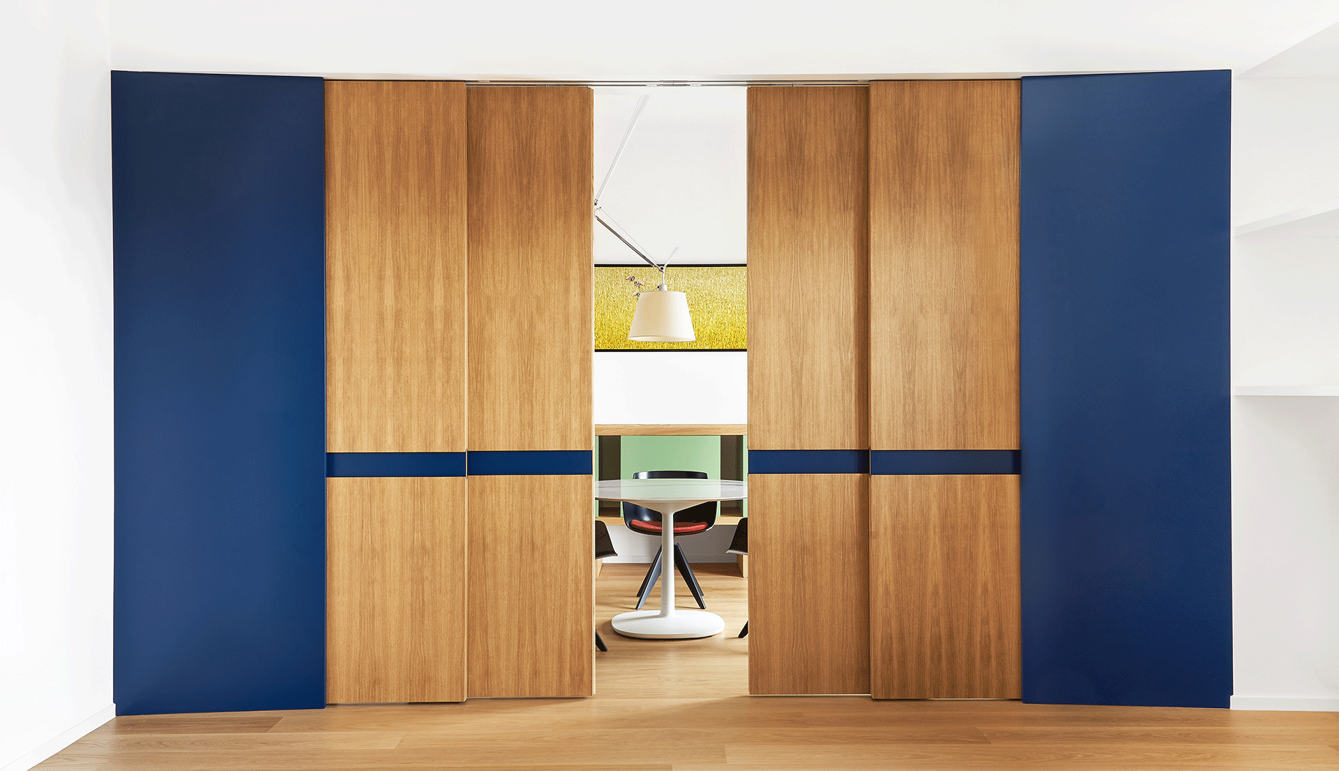 Lampada a sospensione Artemide Tolomeo illumina una moderna sala da pranzo con tavolo rotondo, visibile attraverso pannelli scorrevoli in legno e blu.
