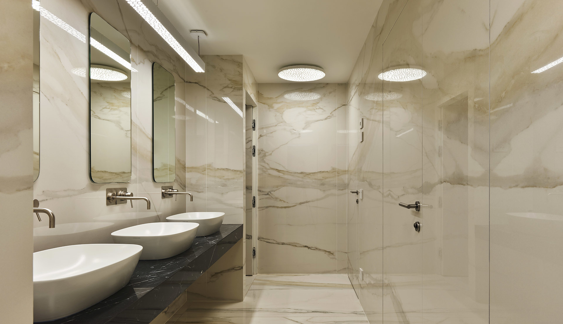 Elegant marble bathroom with Artemide circular ceiling lights over vanity and shower, complemented by linear LED mirror lighting