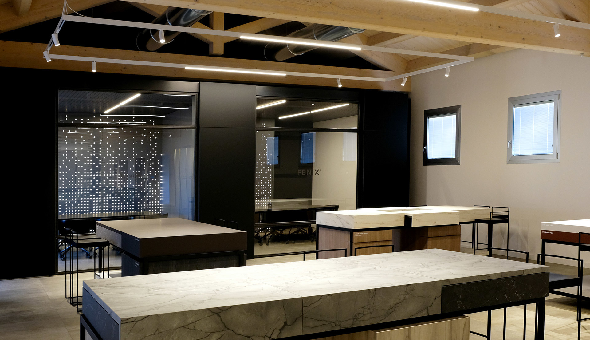 Modern showroom with marble display tables, black wall panels, and Artemide linear LED track lights mounted on wooden beam ceiling.
