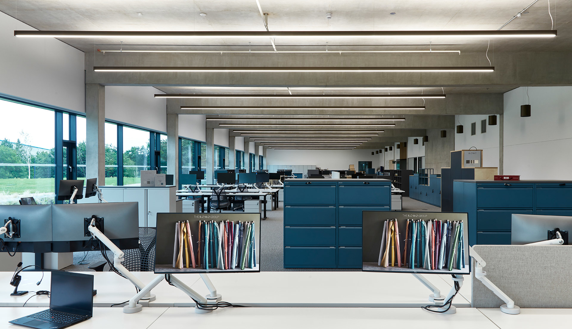 Ufficio open space con file di postazioni di lavoro illuminate da lampade LED lineari a soffitto che garantiscono un'illuminazione uniforme.