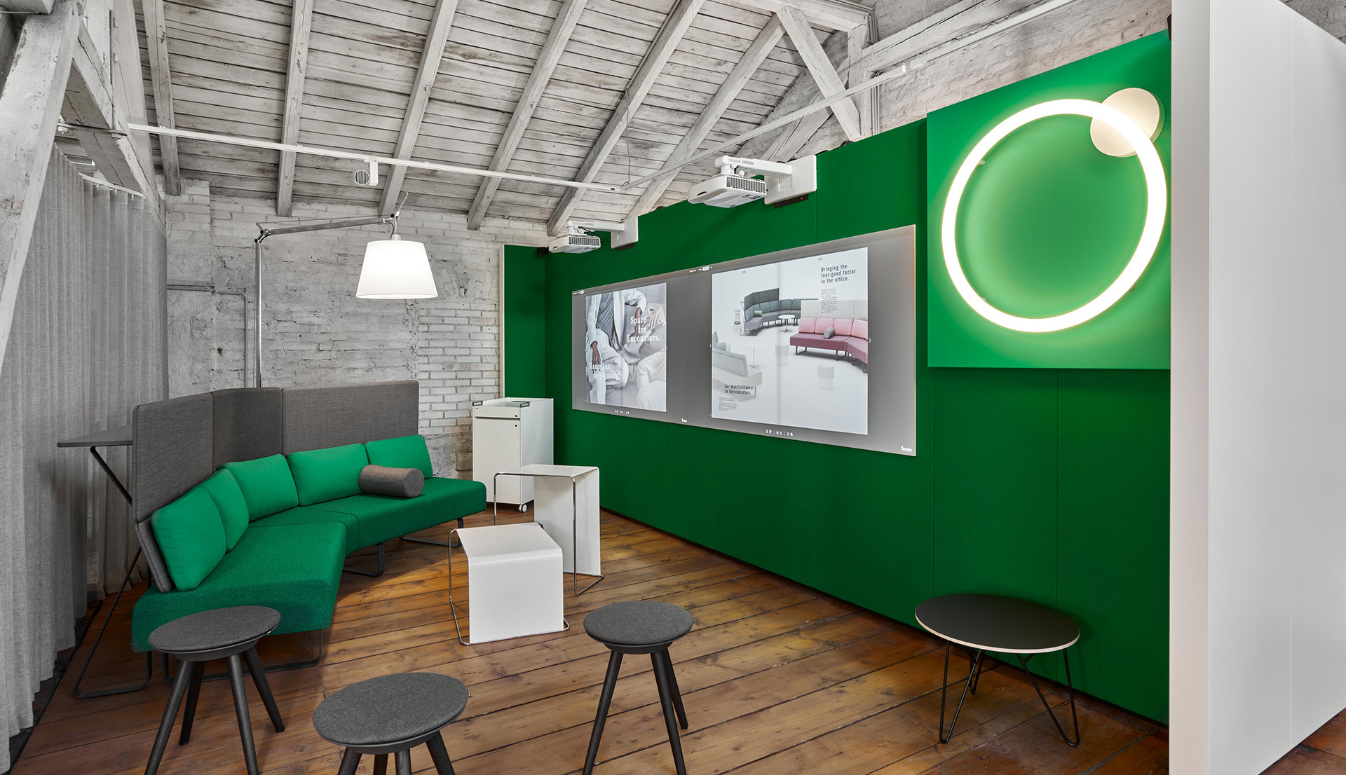 Lounge moderno con divano verde, lampada a sospensione bianca e luce da parete LED circolare su una parete verde con travi in legno a vista.