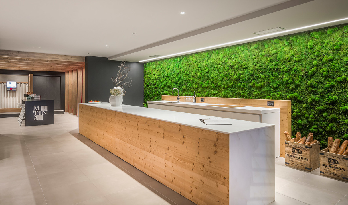 Reception moderna con bancone in legno, parete di muschio verde e luci lineari a soffitto Artemide che illuminano lo spazio.
