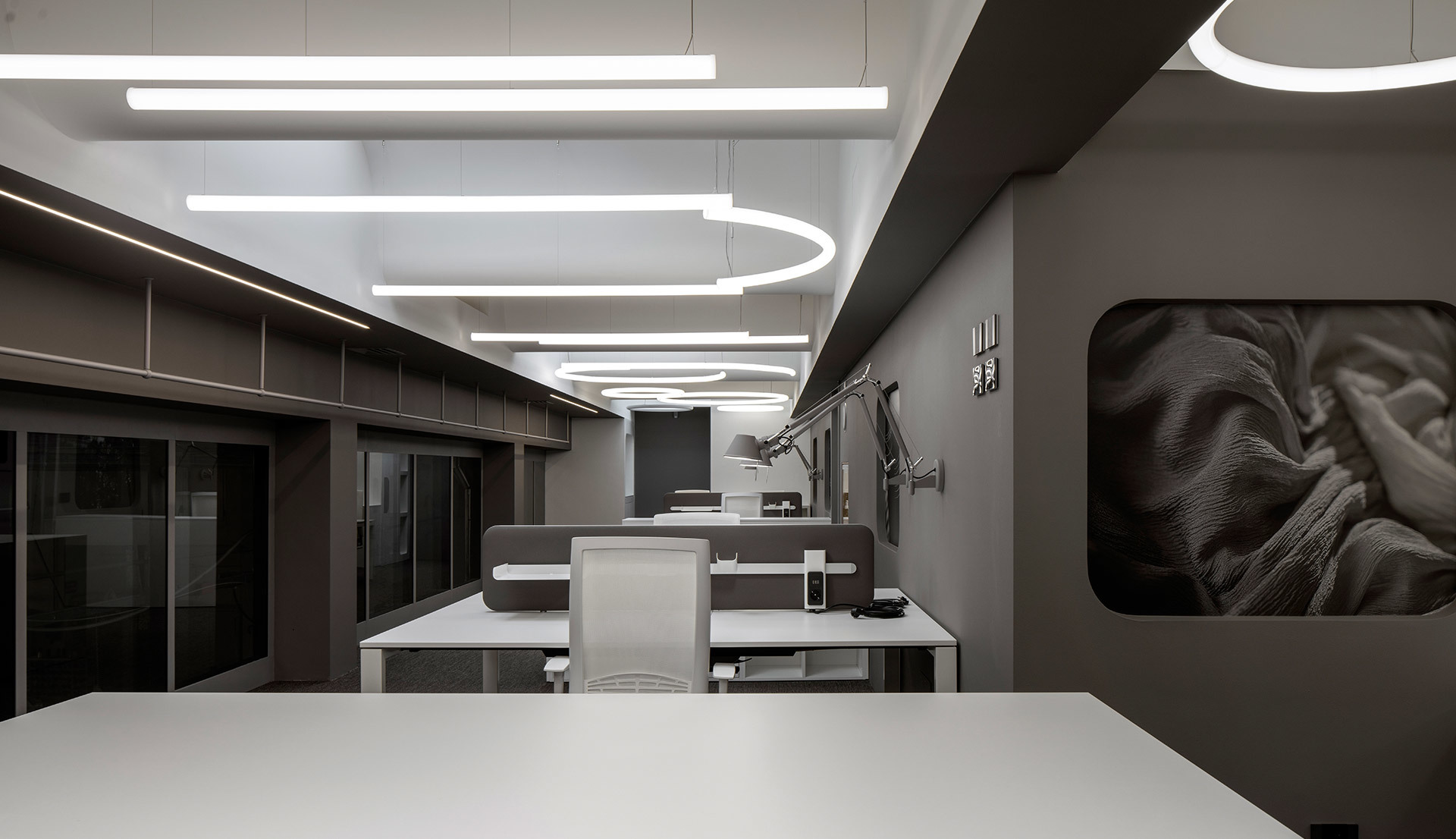 Ufficio moderno con lampade a sospensione lineari e ovali Artemide che illuminano postazioni di lavoro in un elegante interno grigio scuro