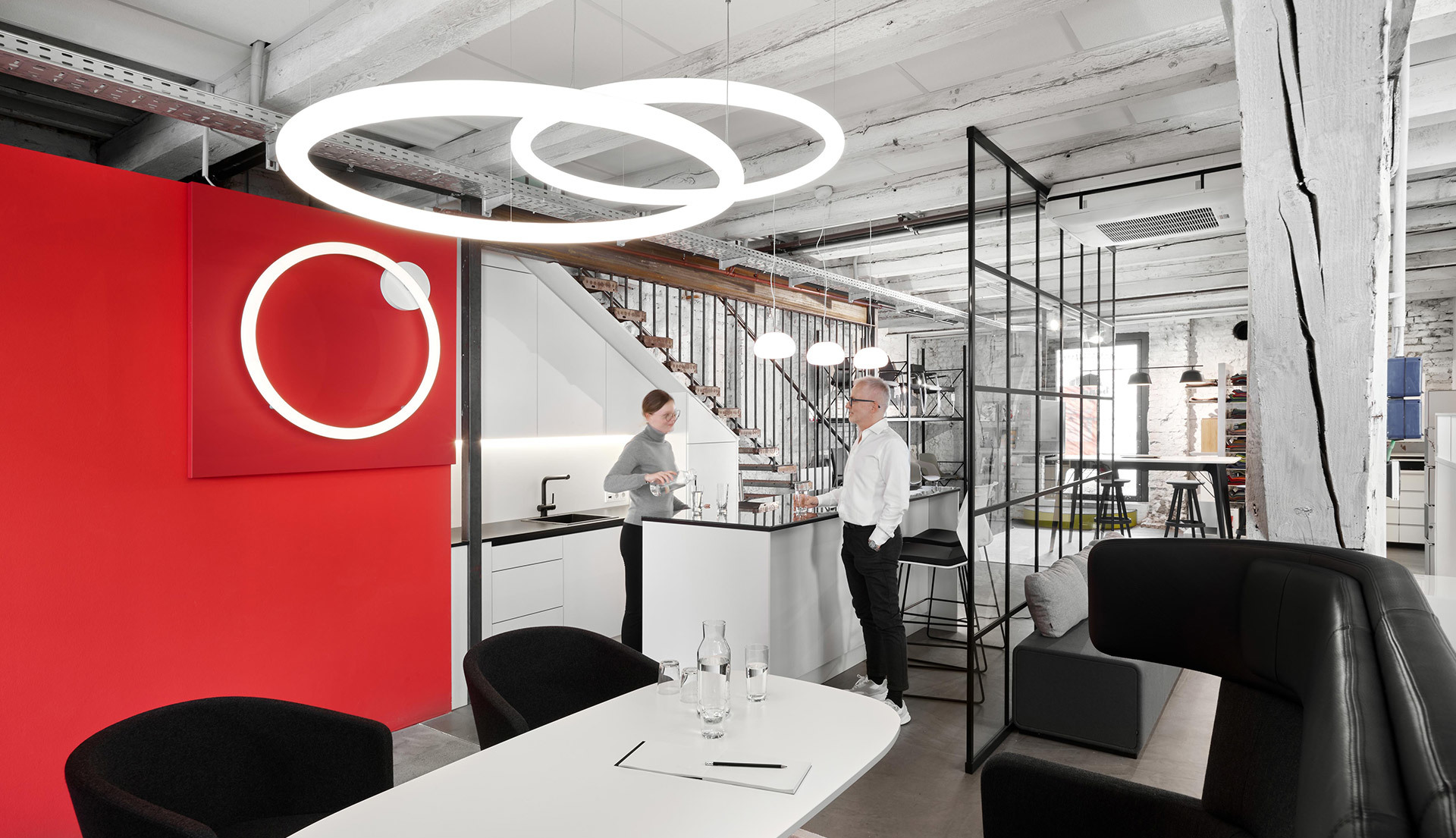 Ufficio moderno con lampada a sospensione Artemide Optical, anelli bianchi intrecciati, sopra un tavolo bianco; parete rossa e interni industriali.