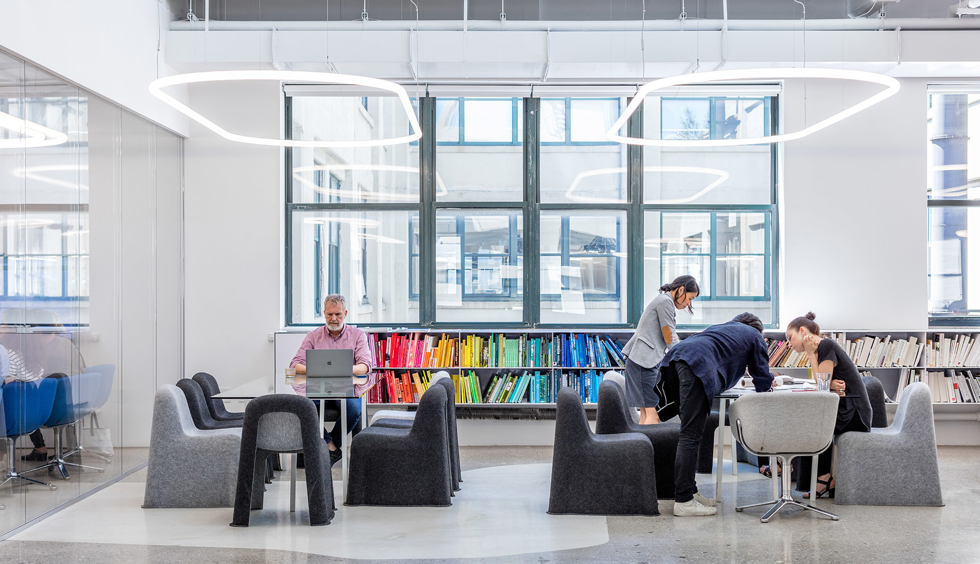 Modern workspace with Artemide circular pendant lights illuminating people working and collaborating around grey lounge chairs and tables.