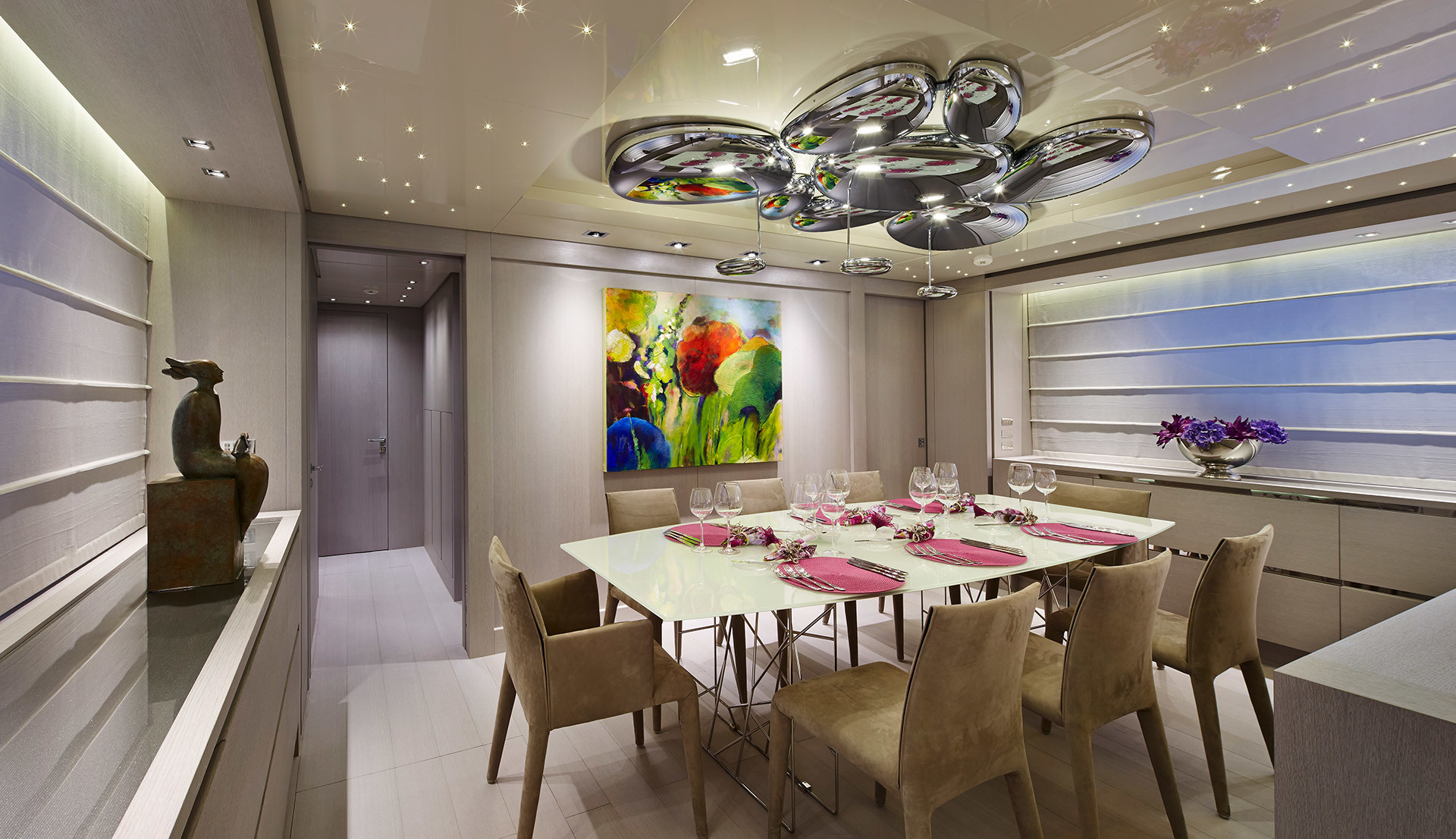 Sala da pranzo elegante con lampada a sospensione a bolle cromate sopra un tavolo bianco apparecchiato con tovaglioli rosa e calici di cristallo.