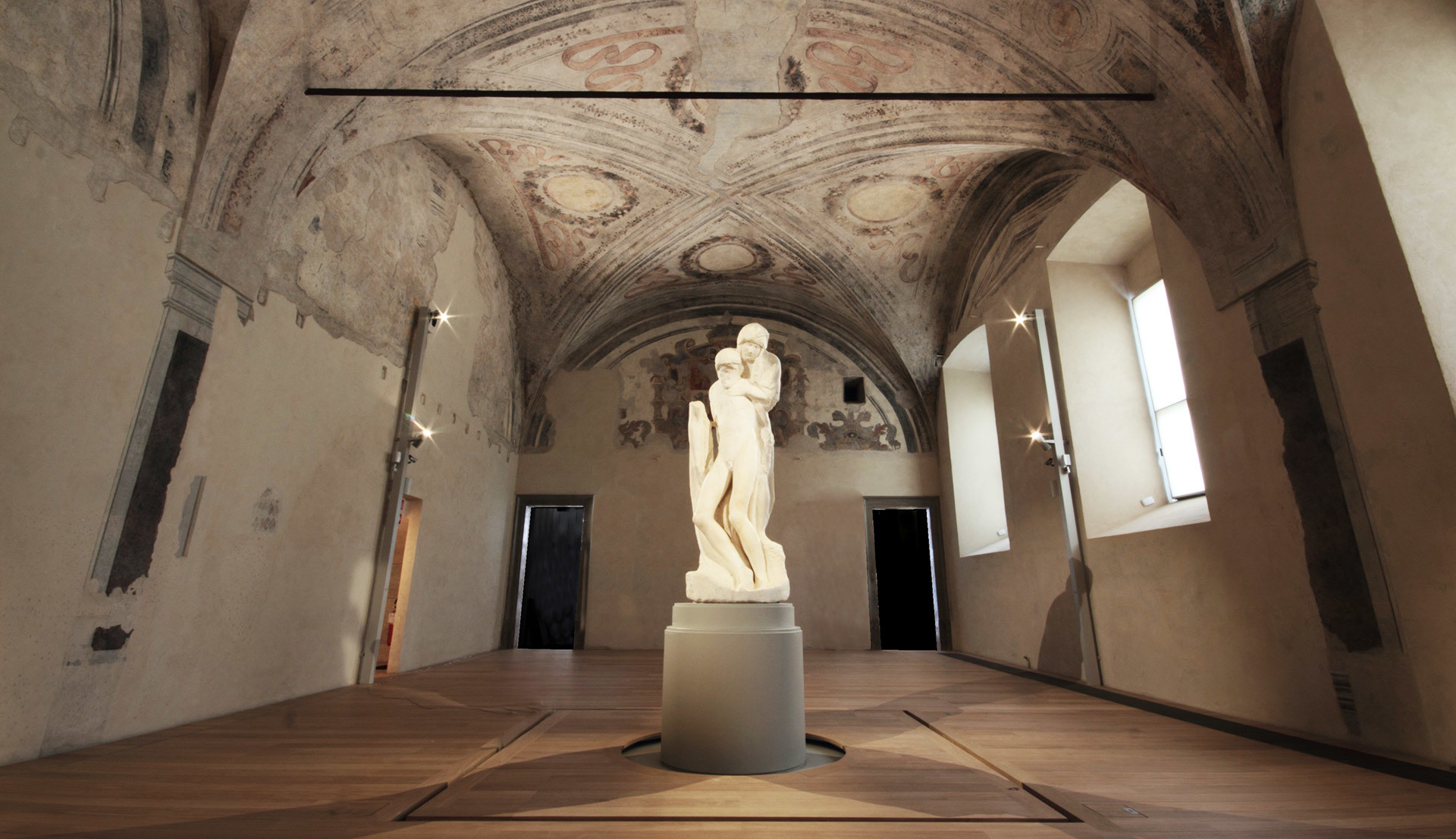 Artemide spotlights illuminate a classical marble sculpture on a pedestal in a historic vaulted hall with frescoed ceiling.