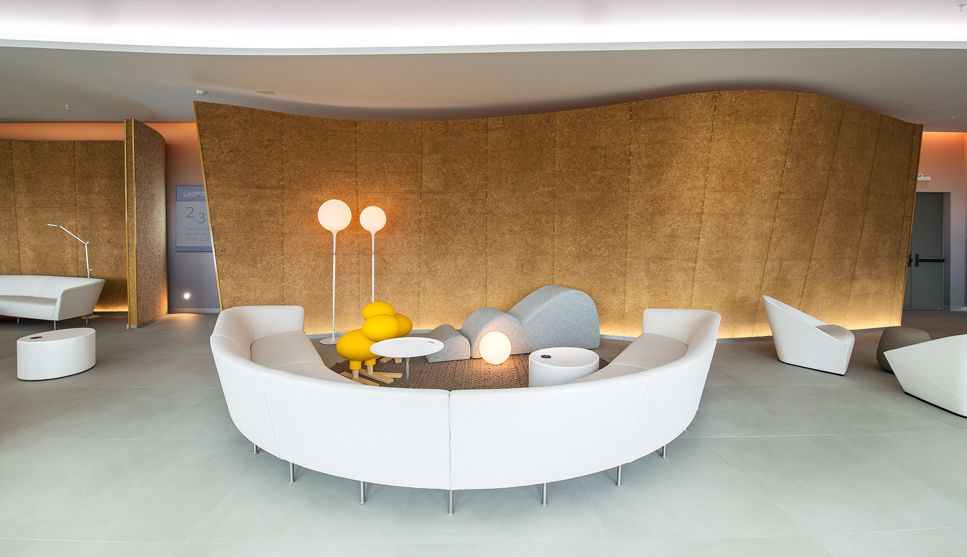 Salotto moderno con divano bianco curvo, lampade da terra gialle con diffusori sferici e parete in sughero illuminata in un interno minimalista