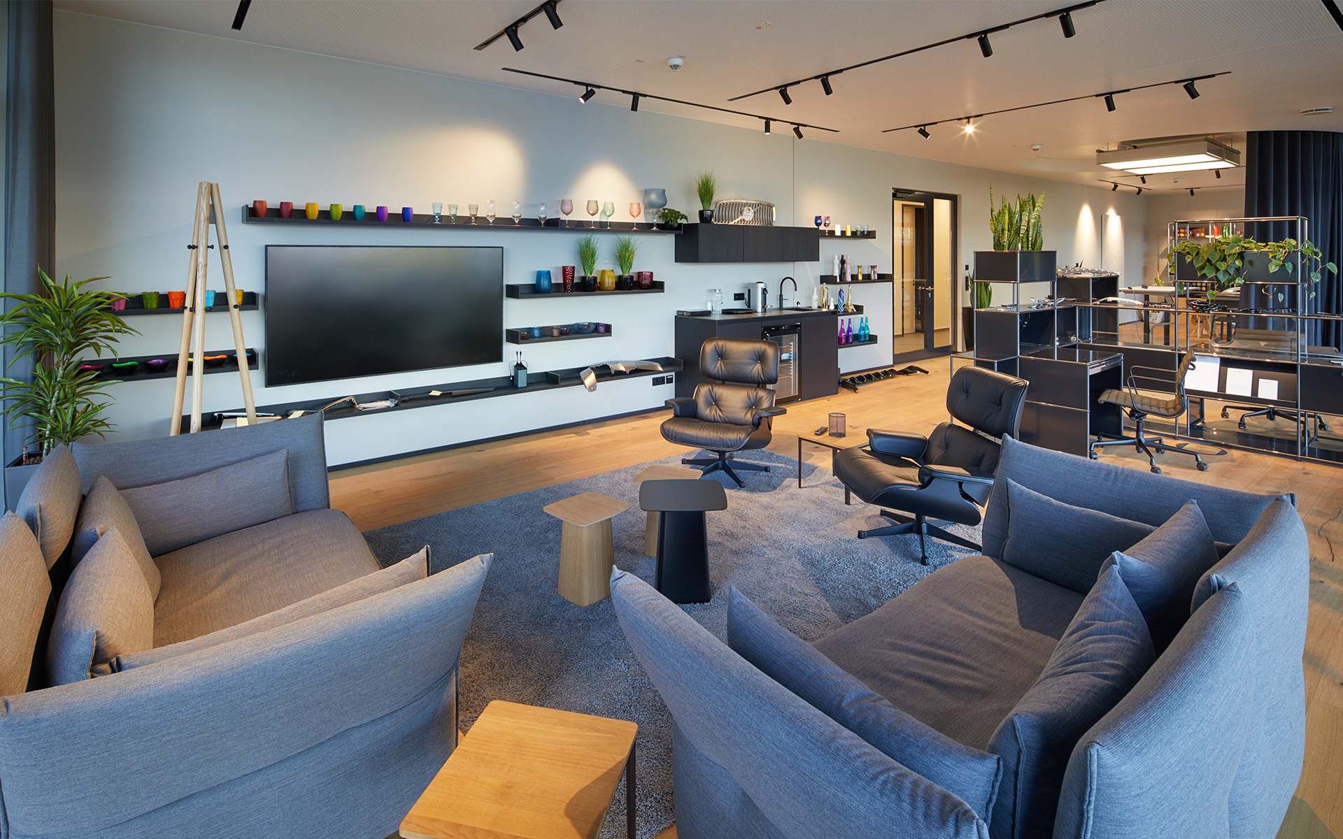 Salotto moderno con divani grigi, mobile TV e faretti a binario Artemide sul soffitto che illuminano un elegante spazio open space