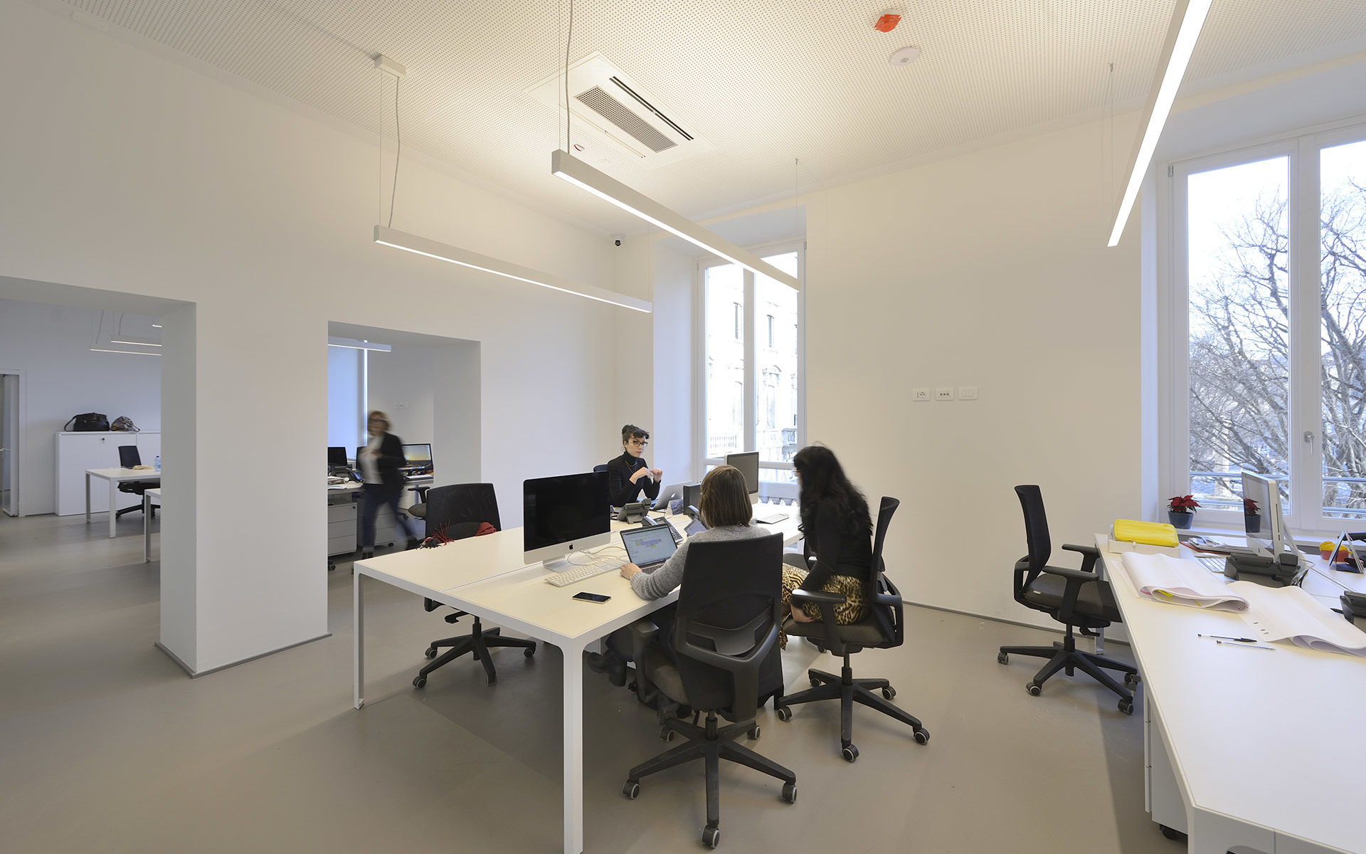 Modern open-plan office with Artemide linear pendant and recessed lights illuminating white desks where people collaborate.