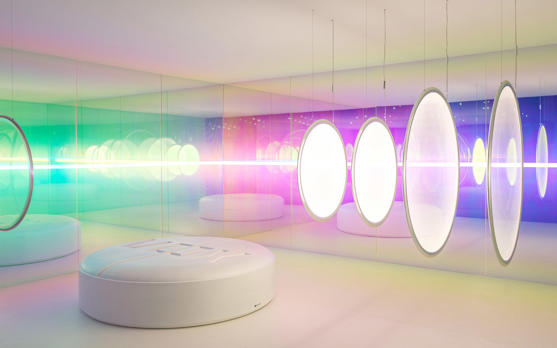 Showroom futuristico con lampade a sospensione ovali che emettono bagliori iridescenti colorati in rosa, verde e viola su pareti bianche a specchio