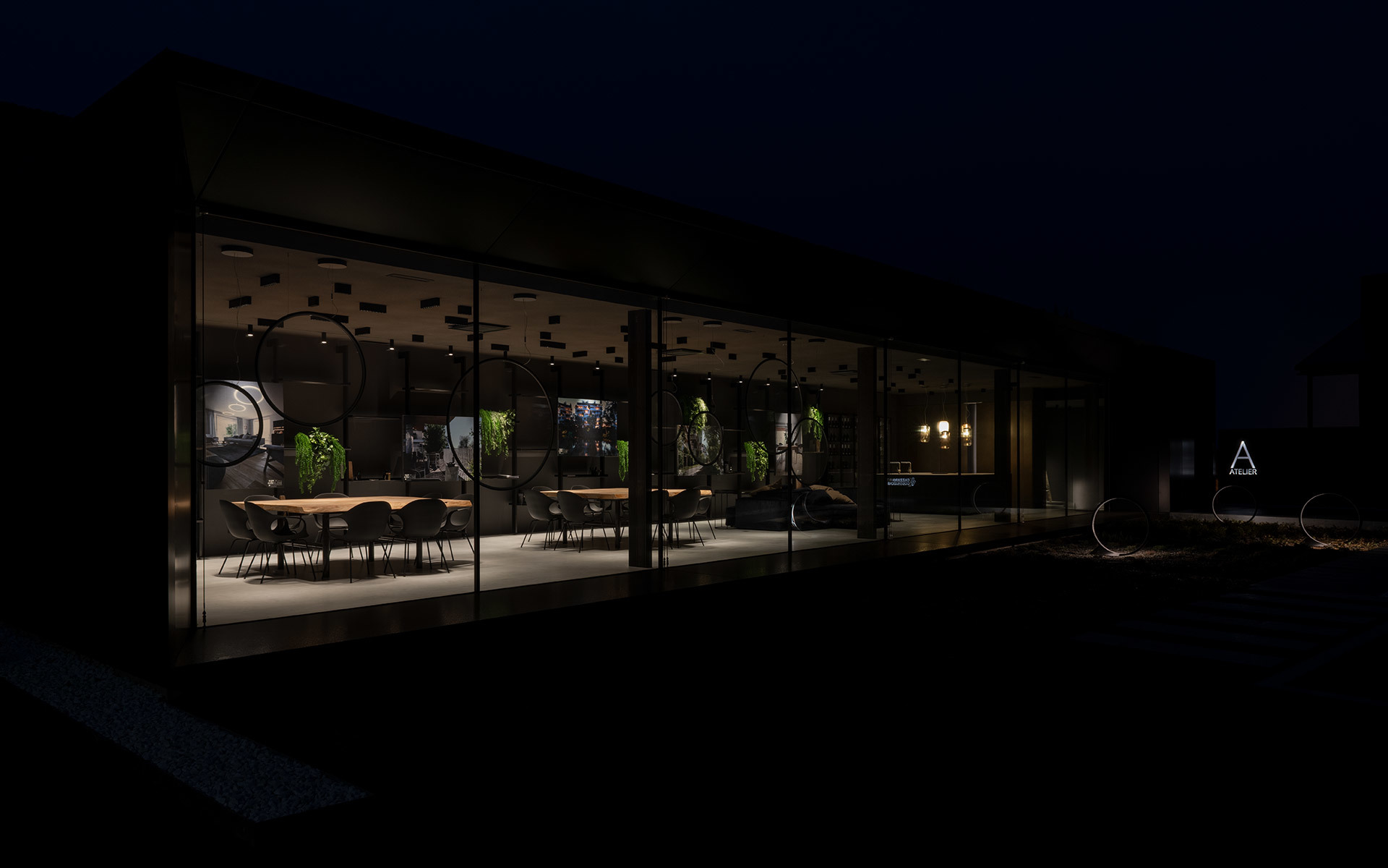 Ristorante o showroom con pareti in vetro illuminato di notte, con lampade a sospensione, piante e un lungo tavolo da pranzo visibile dall'esterno.