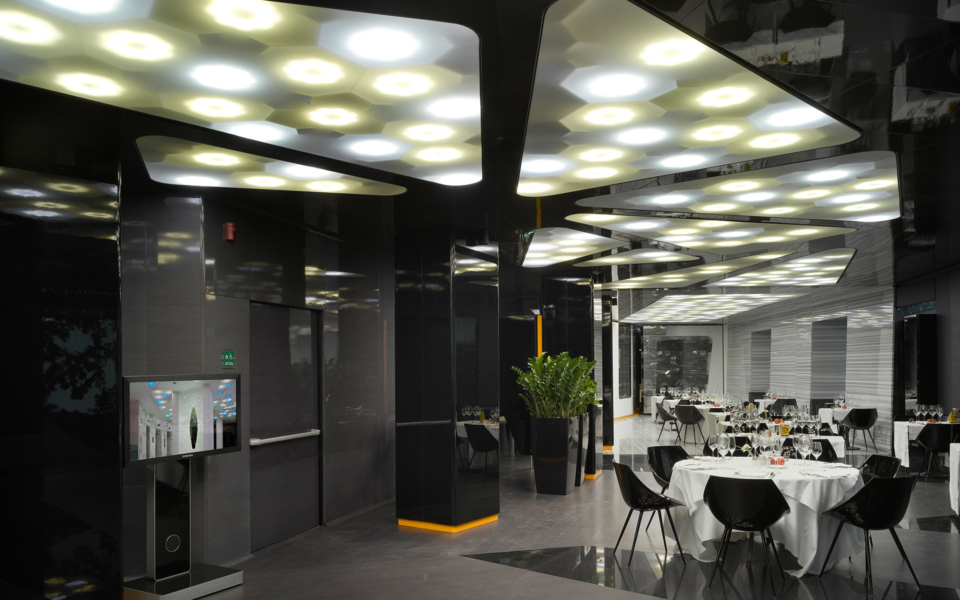 Interno di ristorante moderno con décor scuro e plafoniere Artemide con pannelli LED circolari disposti in schemi geometrici.
