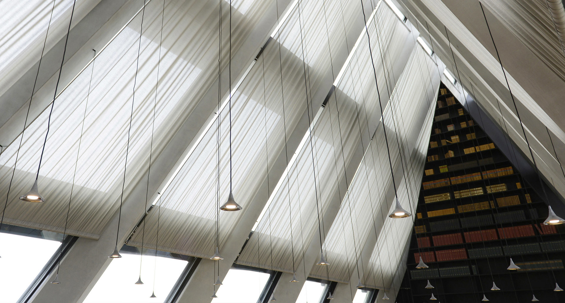 Soffitto interno con spettacolari pannelli diagonali in tessuto bianco e multiple piccole lampade a sospensione appese a sottili cavi in un edificio moderno.