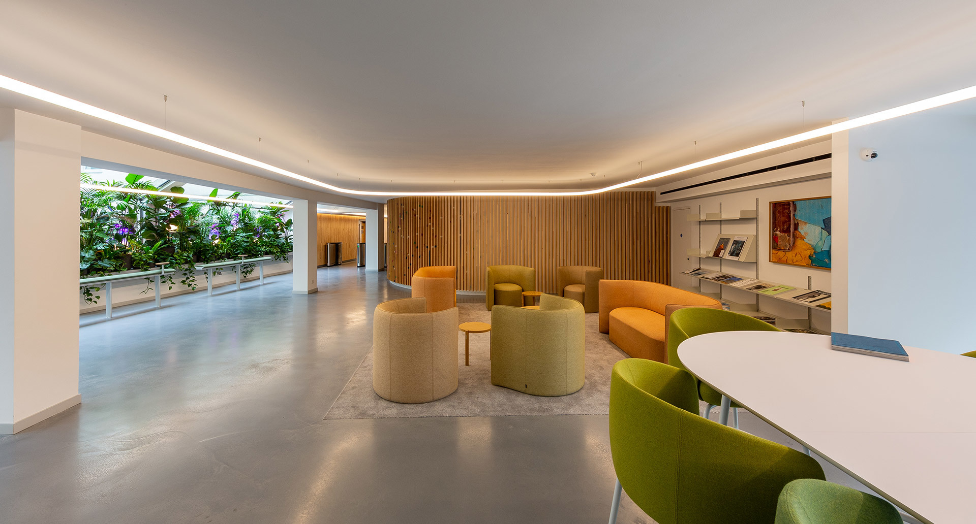 Modern lounge with linear ceiling LED lighting, orange and green seating, wood-paneled wall, and lush garden view.