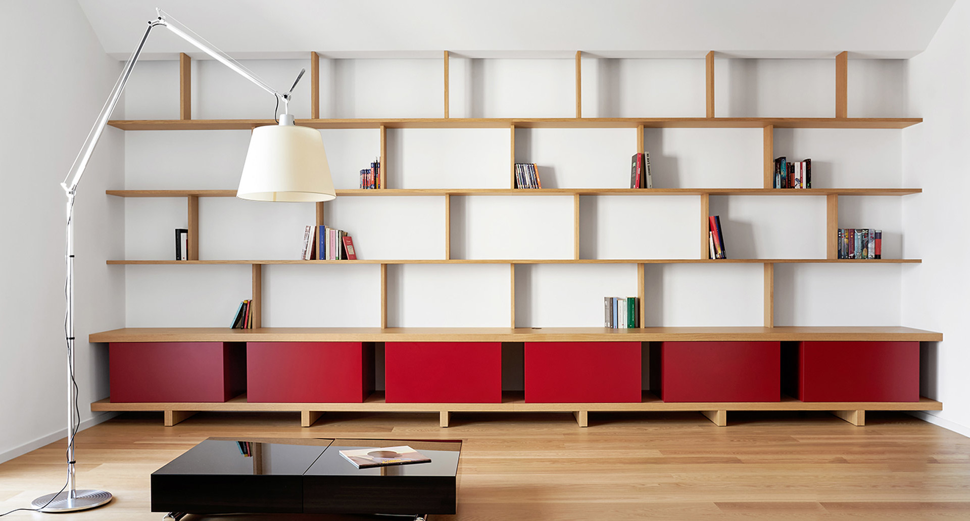 Lampada da terra Artemide Tolomeo Mega con paralume bianco che illumina un soggiorno moderno con grande libreria in legno e ante rosse