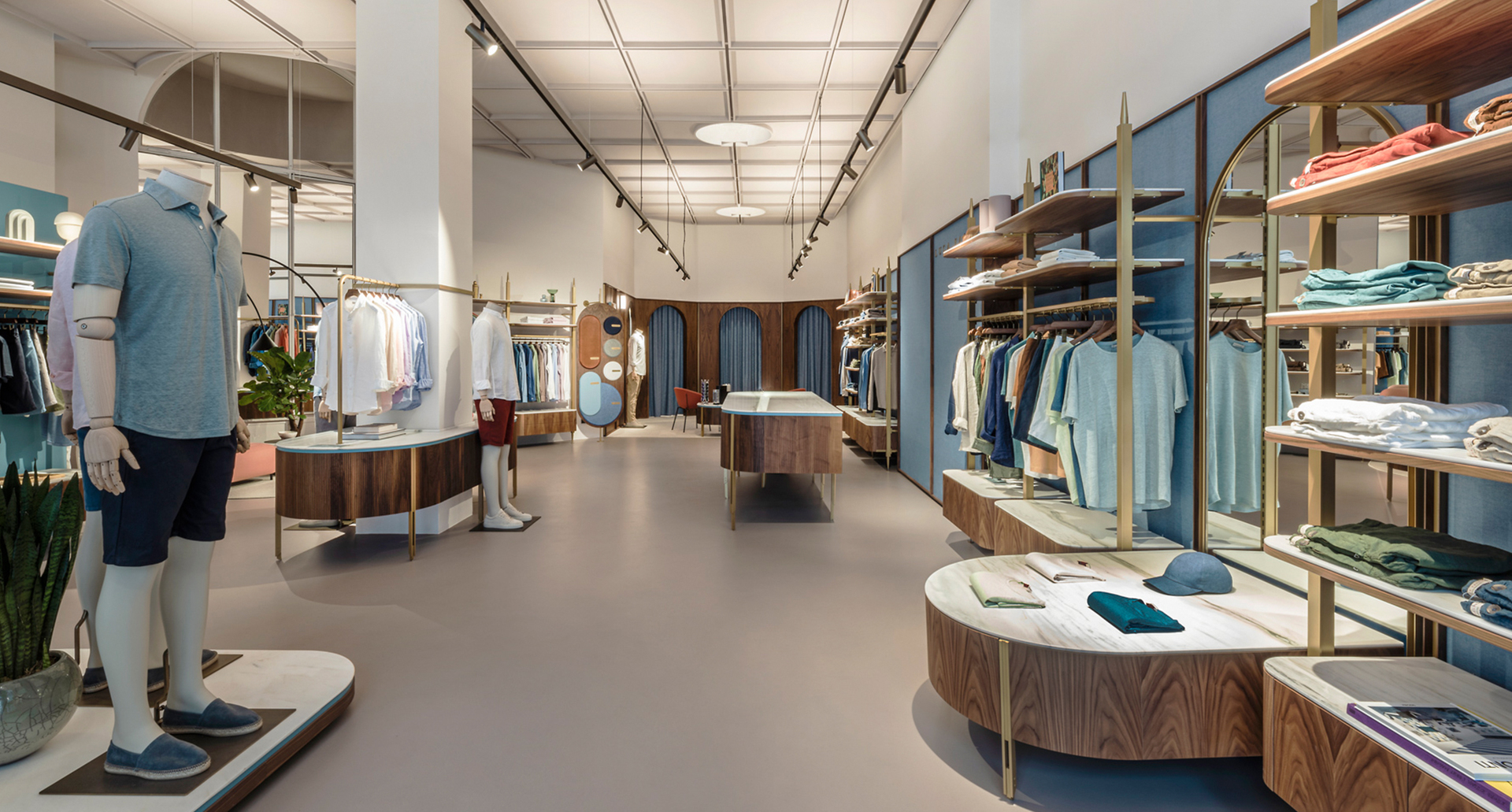 Interno di boutique maschile moderna con faretti su binario e plafoniere a incasso che illuminano espositori di abbigliamento e scaffalature in legno.
