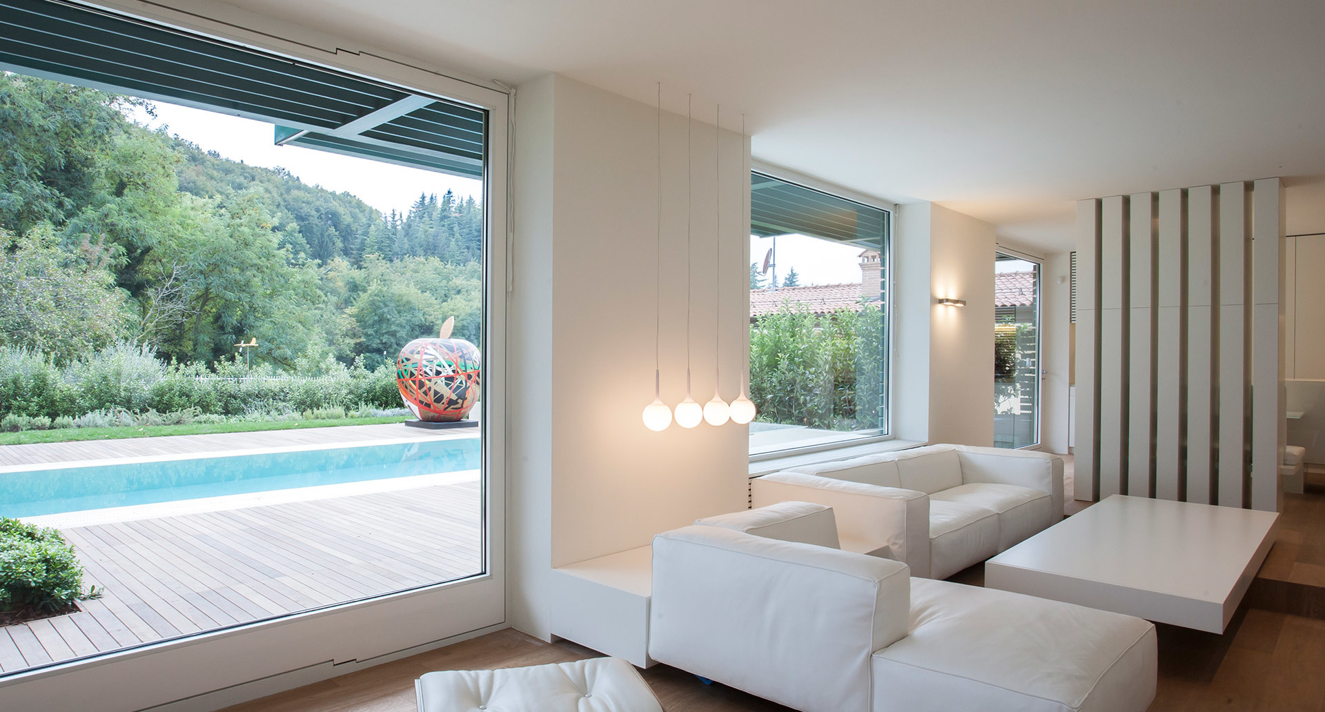 Modern living room with white sofas and Artemide pendant lamp with spherical glass globes, overlooking a pool and garden
