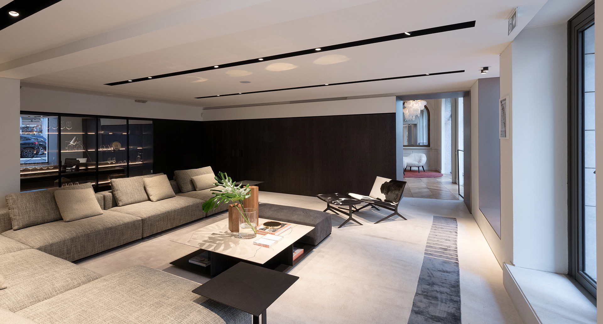 Soggiorno moderno con faretti a soffitto incassati, ampio divano grigio, tavolino nero e design minimalista con parete di accento scura.