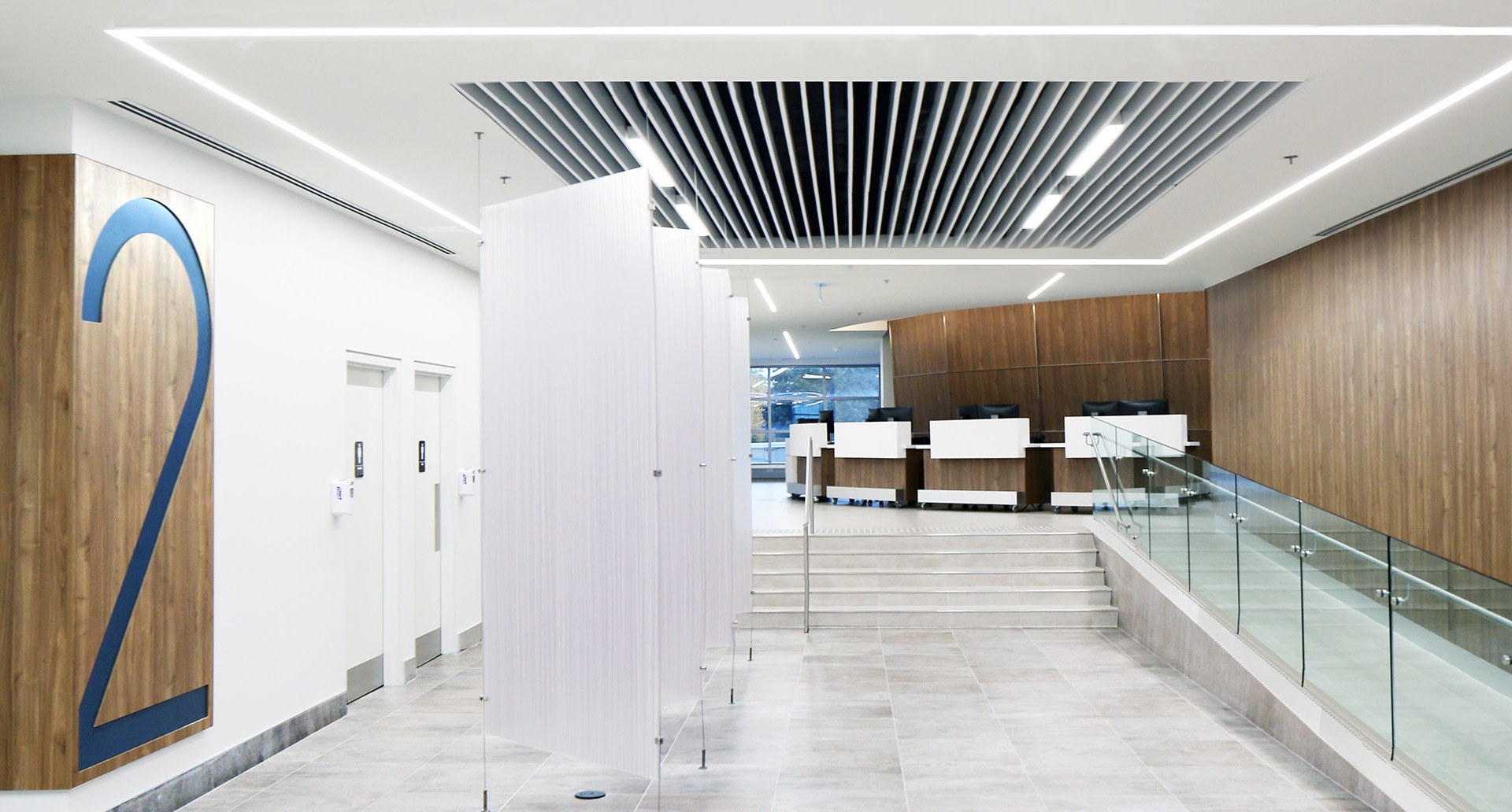 Ingresso di ufficio moderno con luci LED lineari a incasso nel soffitto che illuminano pareti bianche, pavimenti in marmo, pannelli in legno e una reception.