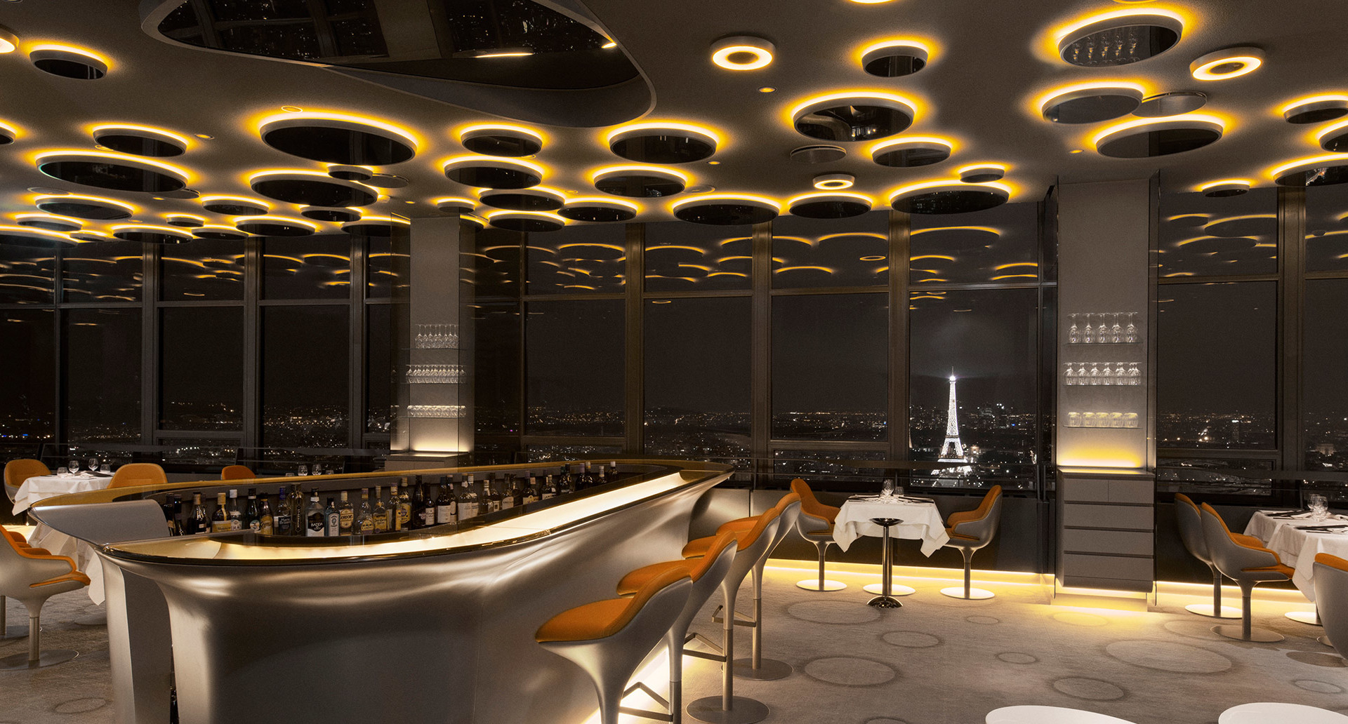 Ristorante di lusso a Parigi con vista sulla Torre Eiffel, soffitto decorato da anelli LED circolari Artemide con luce dorata calda